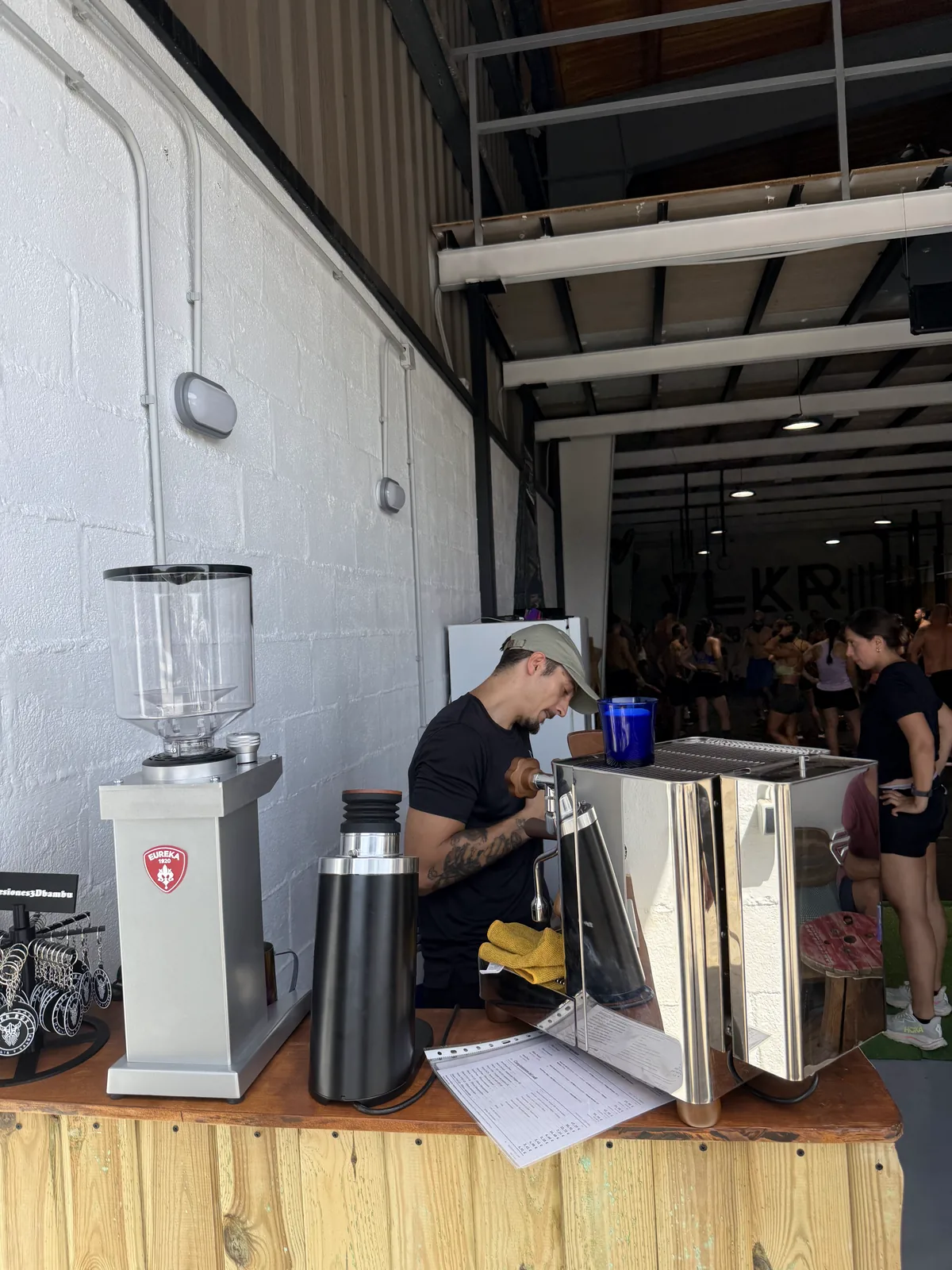 Barra de degustación de café de especialidad de Naos Coffee con el interior del box de CrossFit y los asistentes al fondo.